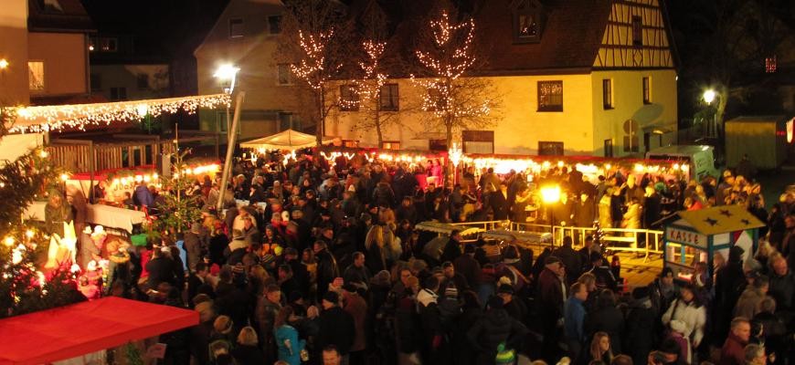 Blick über den Weihnachtsmark bei Nacht Beleuchtete und geschmückte Stände und eine Menschenmenge bei Nacht